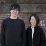Playfool写真。レンガの壁の前に立ち笑う男女１名。受かって左が男性（ダニエル）、右が女性（さき）