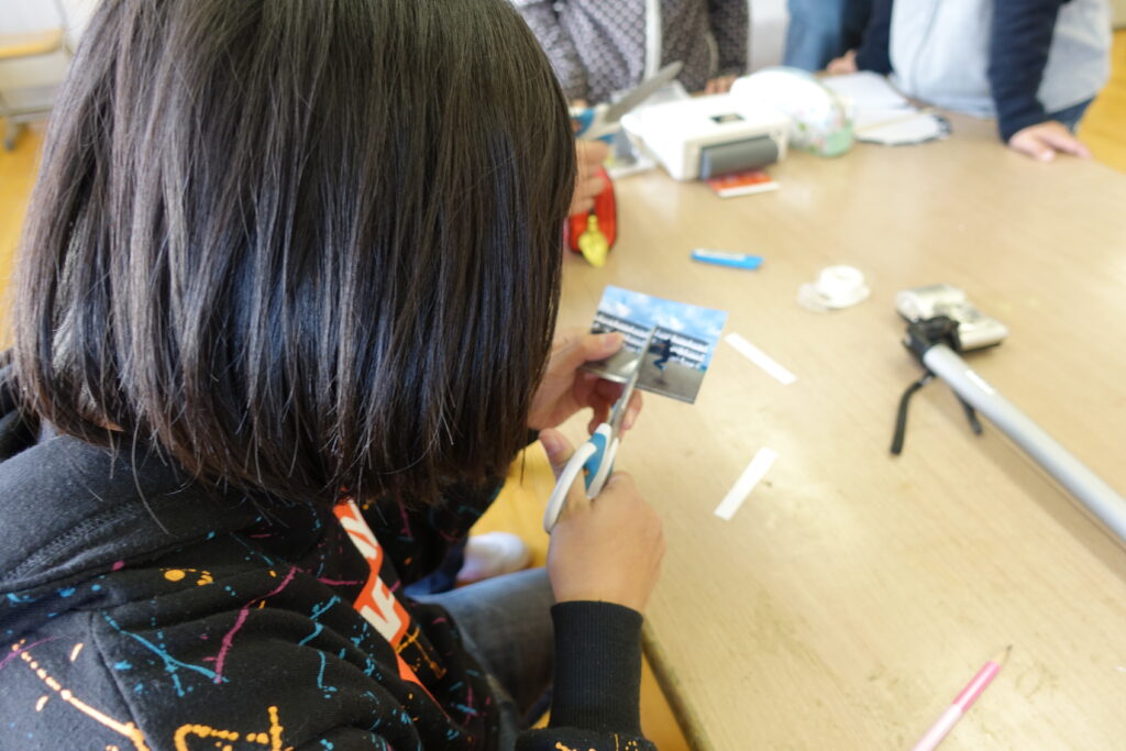 橋本さんが小学校で行われたプラクシノスコープワークショップ。
子供達がチームでプラクシノスコープを組み立てている。
ハサミを使って装置の大きさに合わせて写真をカットする。