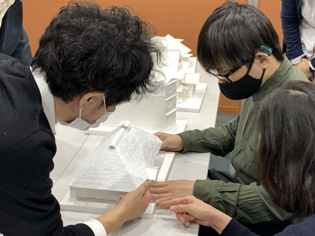 テーブルの上に置かれた建物の模型を手で触れて調べている様子